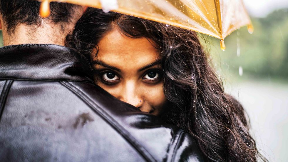 Multiethnic couple of lovers hugging under the umbrella on a rainy day. (Shutterstock)