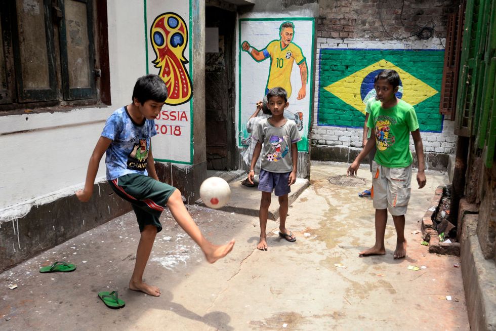 Indian boys play football or soccer barefoot in a narrow lane of Kolkata in front of Brazil flag and player Neymar (Jr.) painted on wall on the occasion of FIFA World Cup 2018. (Photo by Saikat Paul/Pacific Press/LightRocket via Getty Images)