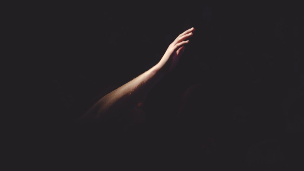 A depressed person with their arm reaching out in the blackness. Photo by Cherry Laithang on Unsplash