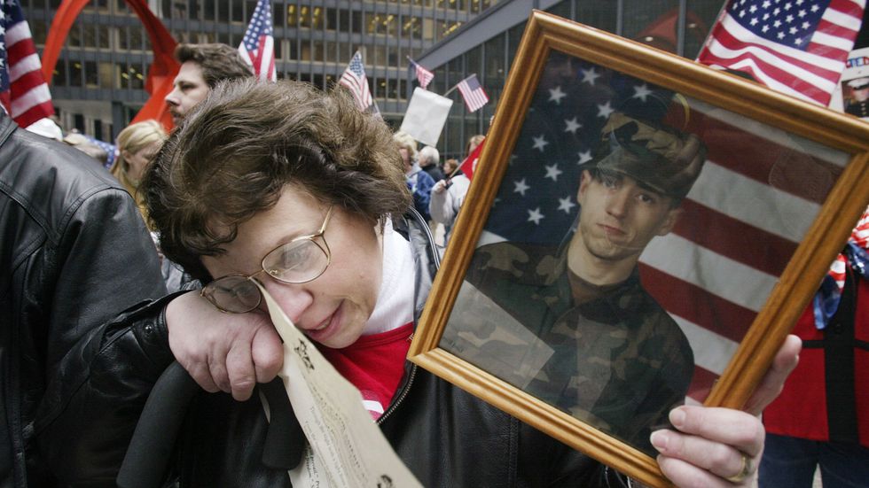 Claire Tortorello, holding a photo of her son Greg, wipes a tear from her eye following the singing of a patriotic song during a war protest March 22, 2003 in downtown Chicago, Illinois. (Photo by Scott Olson/Getty Images)