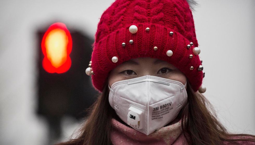 A Chinese woman wears a mask to protect against pollution as they wait to cross the street in heavy smog on December 8, 2015 in Beijing, China. (Photo by Kevin Frayer/Getty Images)