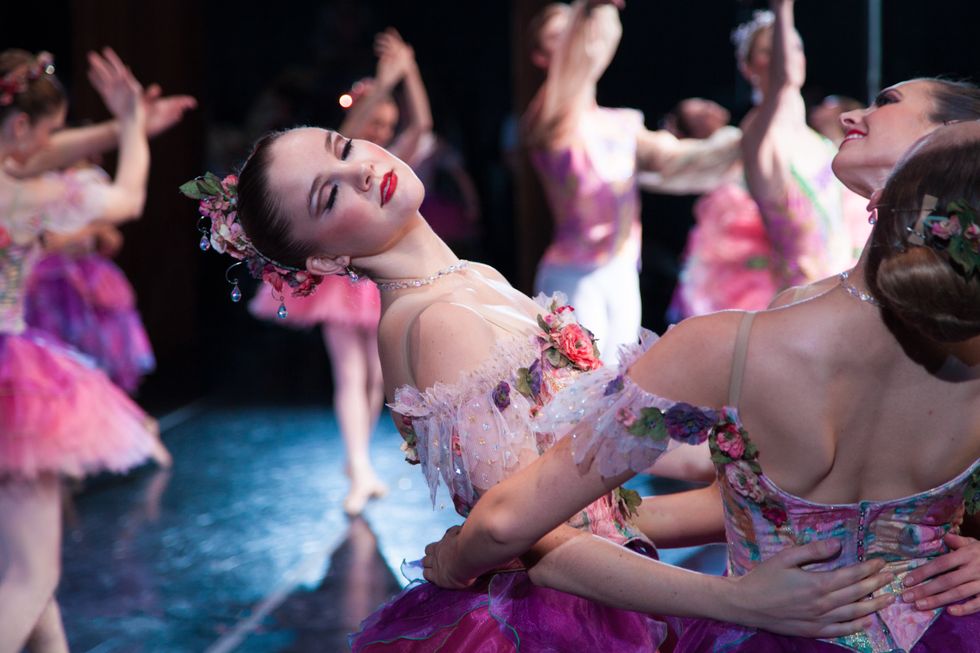 A group of dancers in pink Nutcracker flower costumes hold each other's waists and lean back. Paige Adams, center has her eyes closed.