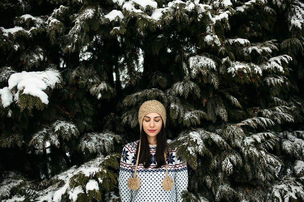 A woman with a winter hat standing surrounded by pine trees covered with snow