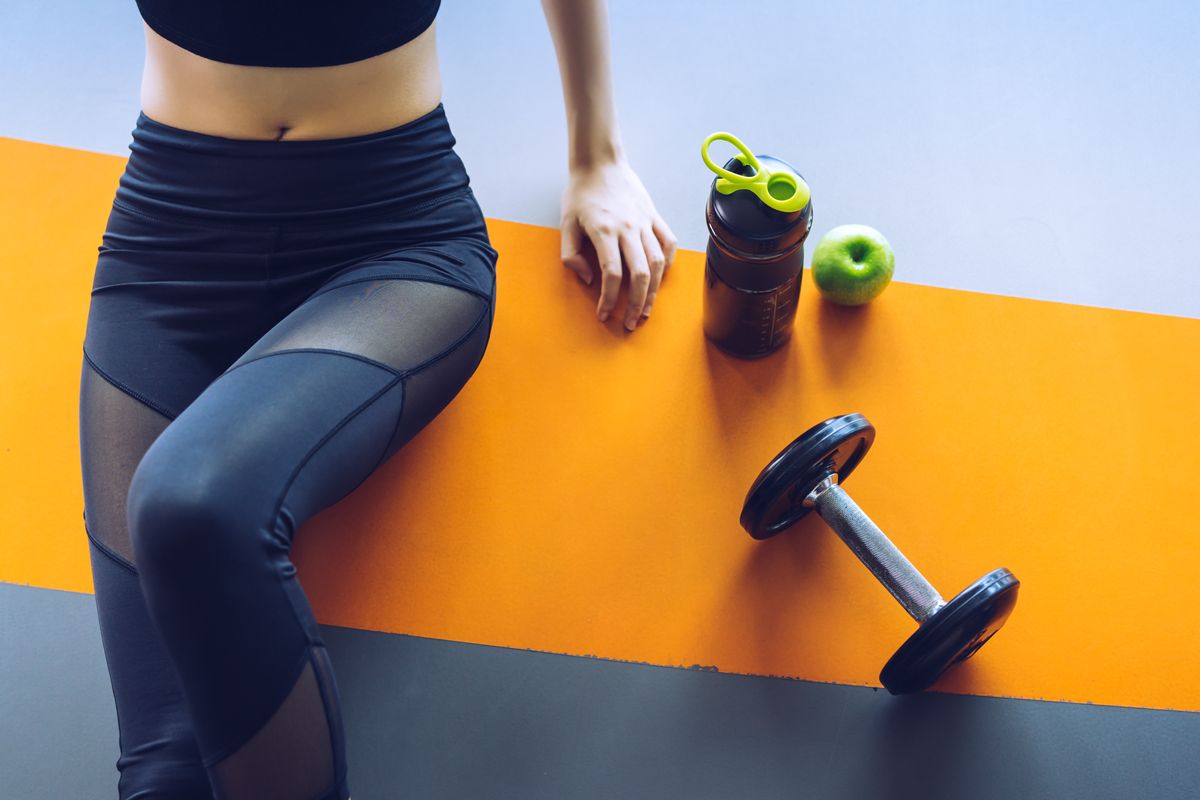 woman sitting on yellow yoga mat with an apple, barbell and apple