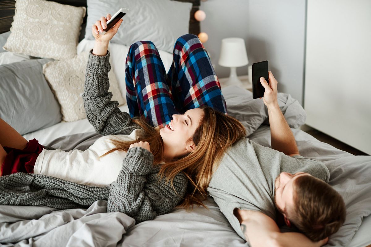 a couple lying in bed laughing while they look at phones