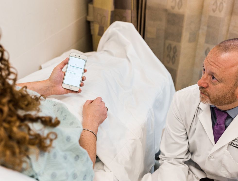 Doctor talking to a patient in a hospital bed with iphone in her hand.