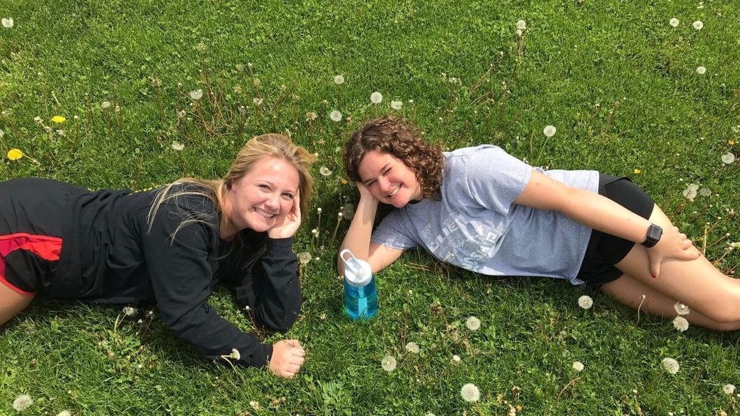 two smiling college girl best friends lying in field
