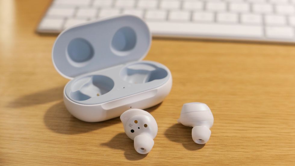Two white earbuds on a table from Samsung, next to its case