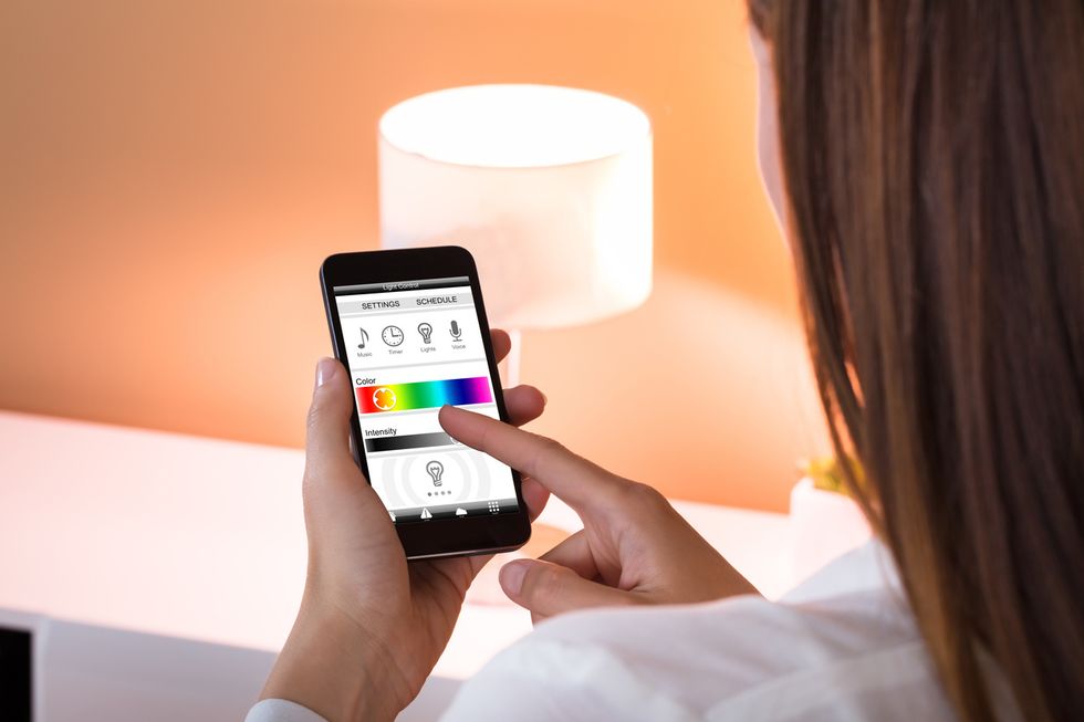 Photo of a woman holding a smartphone and operating a smart light through an app