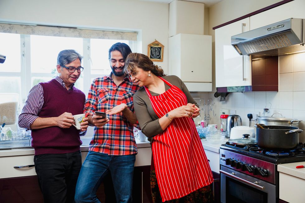 A photo of two parents and an adult child looking at something on a smartphone in a home