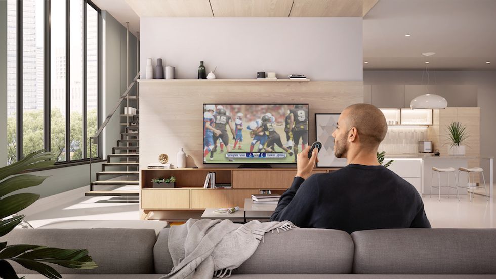 A photo of someone at home using the new Logitech Harmony Express controller, which lets you access Alexa to run your smart home entertainment by pushing the center button