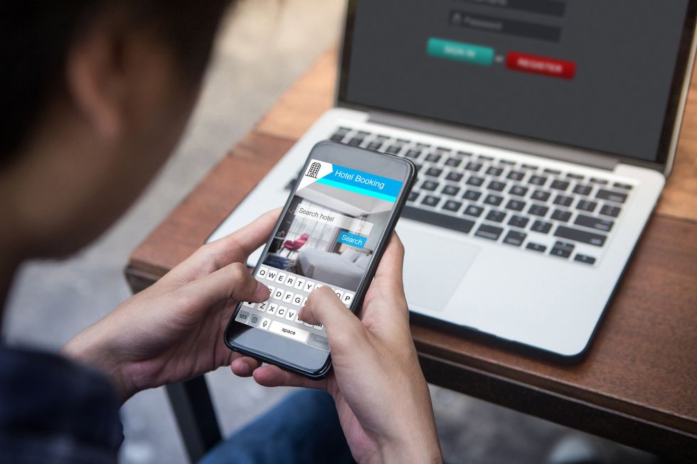 A photo of someone booking travel on their smartphone with a laptop open