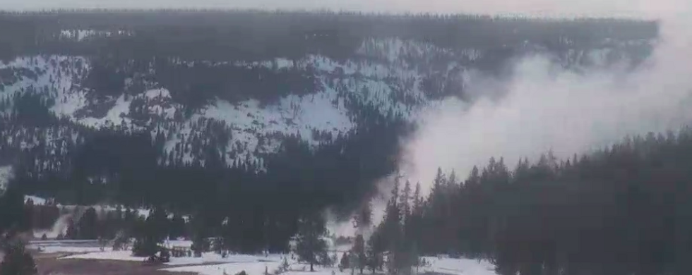 A photo of Old Faithful geyser erupting at Yellowstone National Park with snow on the ground