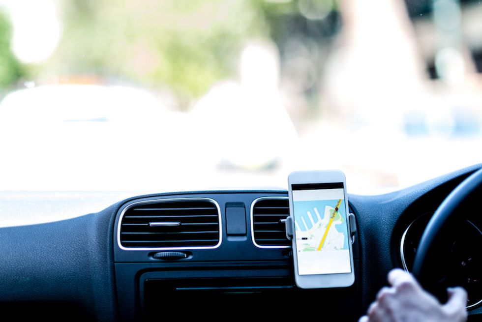 Photo of a smartphone with directions on its screen with a driver in the car