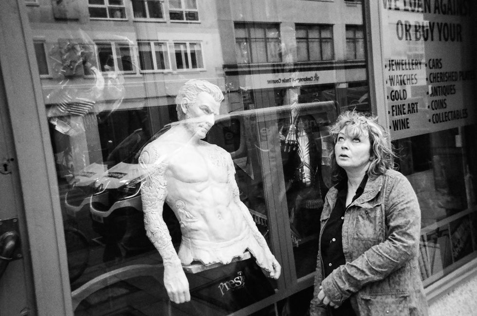 a woman rolls her eyes at a mannequin through a window