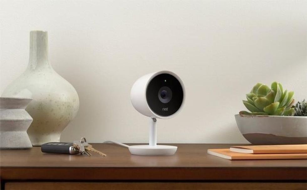 An image of a smart security camera from Google Nest seated on a wooden table next to keys and a succulent