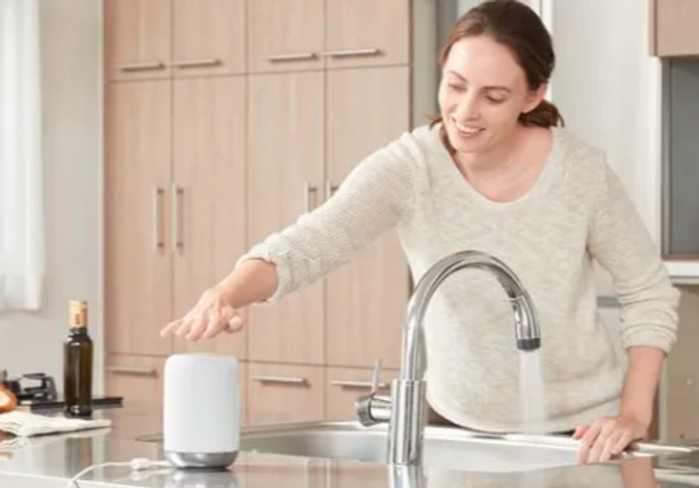 Photo of a woman in a kitchen with Sony LFS50G/W smart speaker with Google Assistant built in.