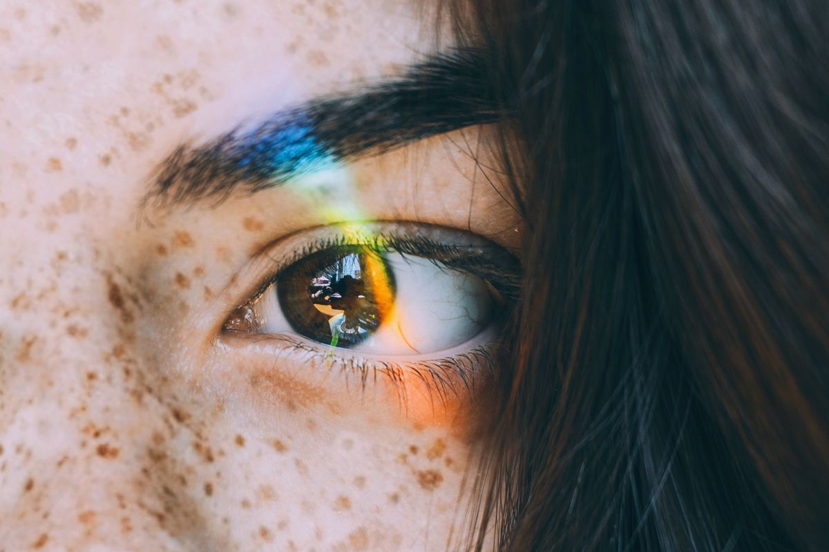 A rainbow shines on the eye of a freckled, brown-haired girl