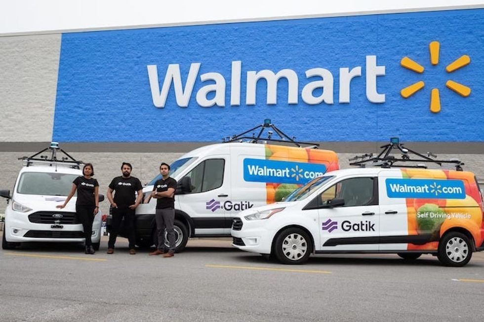 Gatik autonomous vans with Walmart logo across them in a parking lot under a Walmart store sign
