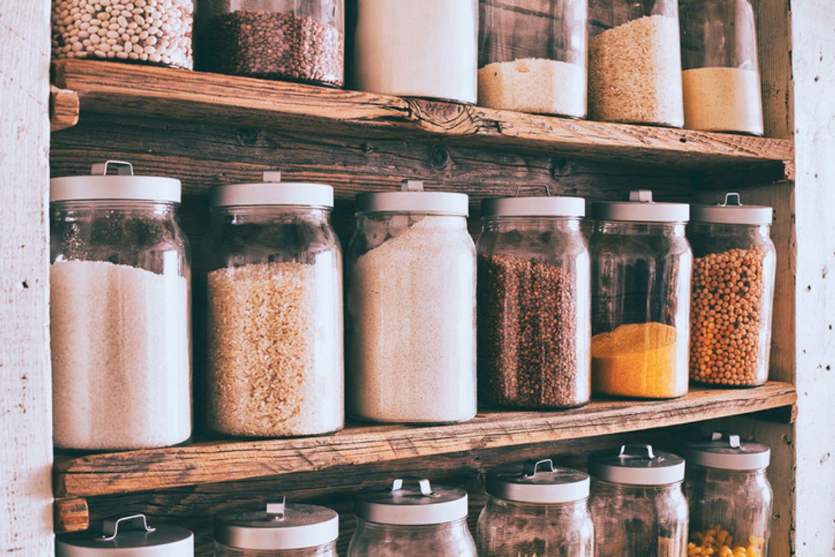 On two shelves, there are rows of clear jars filled with different grains and seeds
