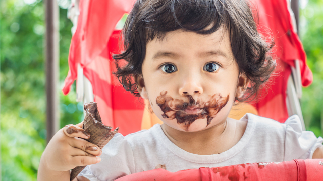 Child with chocolate-covered face holding an ice cream cone.