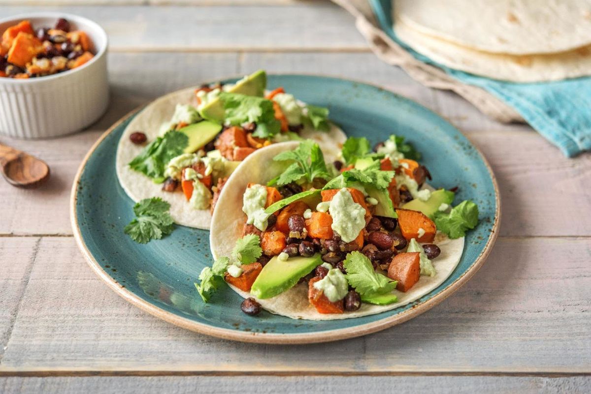 Two tacos filled with beans, avocado and sweet potatoes on a blue plate