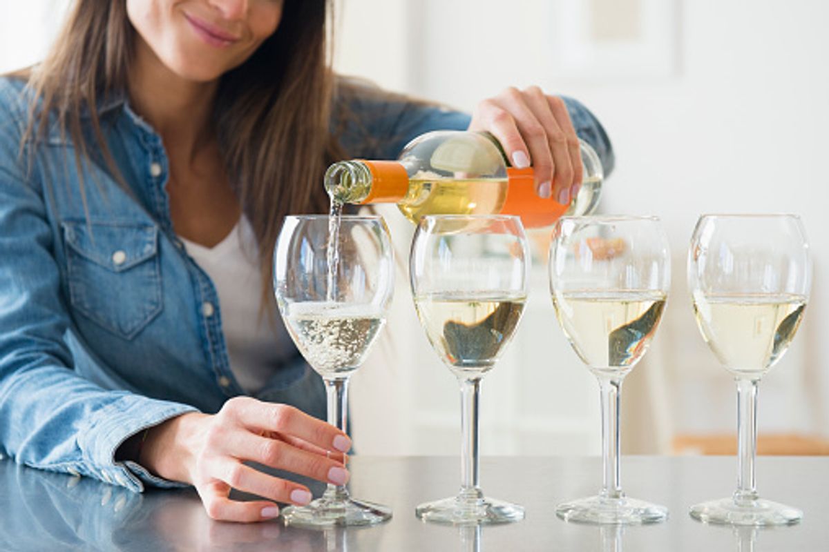 A brown-haired woman pours white wine into 4 glasses