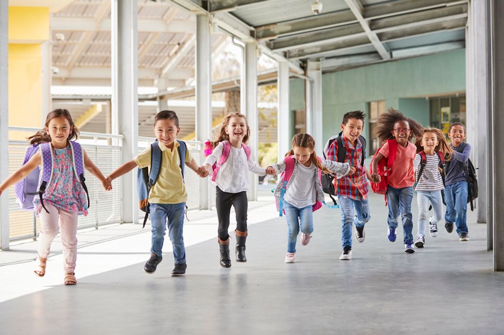 Young children holding hands and laughing running through a school hallway