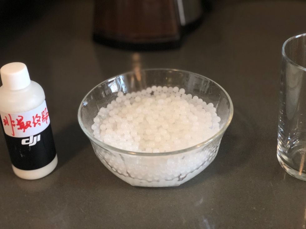 Gel beads soaked in water in a glass bowl on a counter next to a bottle with the letters "DJI" on it