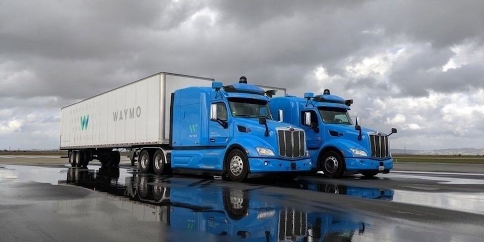 A photo of a two Waymo trucks, both with a blue cabs and white truck