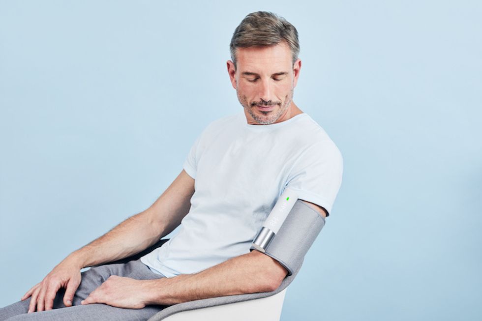 A photo of a man, seated, in a white T-shirt and gray pants wearing a gray cuff that covers half his upper arm