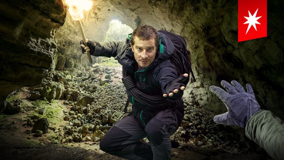 A man holding a torch and wearing a backpack standing in a cave with his hand reaching out
