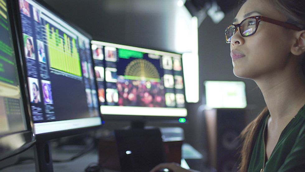A woman wearing glasses staring a three computer with people's faces visible on the screens