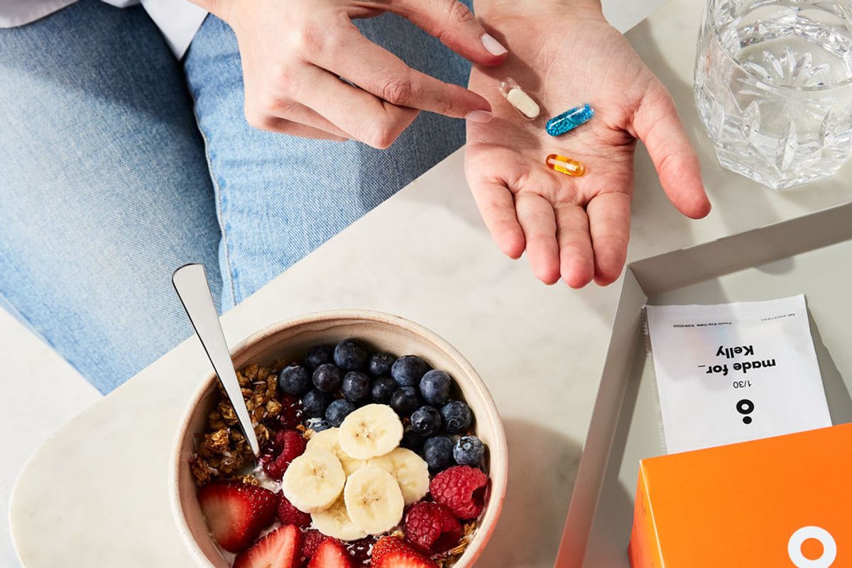 woman having granola for breakfast about to take her vitamins in hand