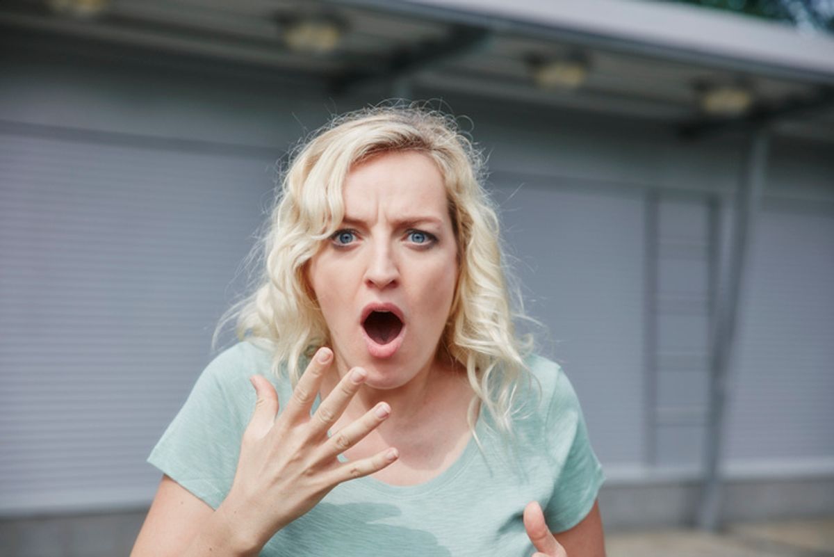 A blonde woman in blue gasps and holds her hand to her mouth