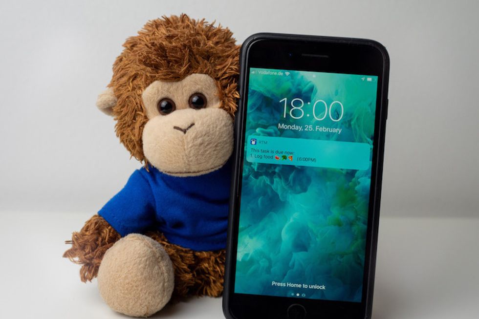 A stuffed animal shaped like a monkey next to a smartphone with a reminder on the screen