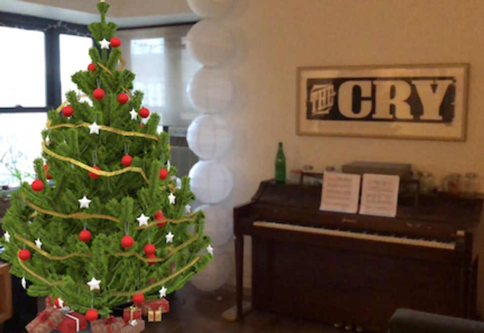 A digital Christmas tree in a living room, next to a piano and a sign that reads "The Cry"