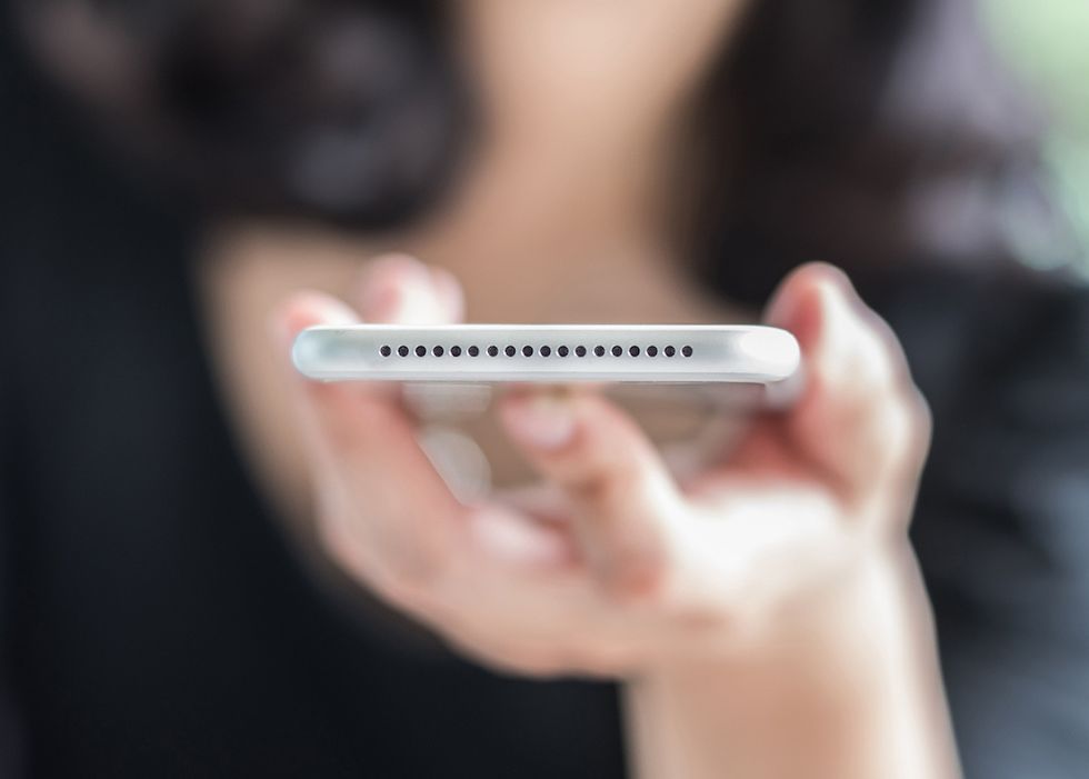 A hand holding a white smartphone, with the speaker pins facing outward