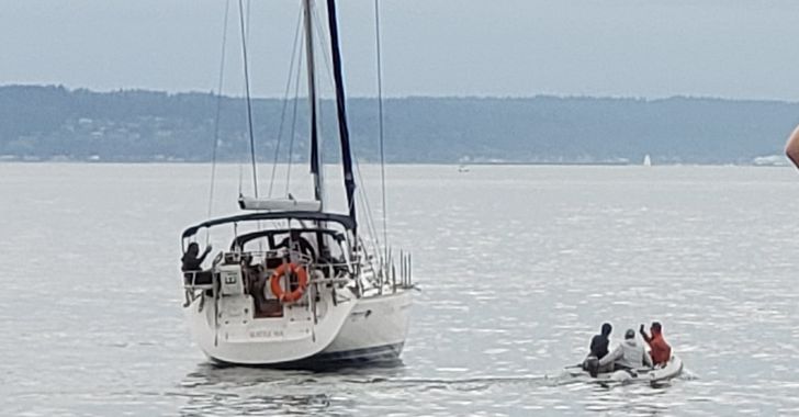 Sailboat on Elliott Bay with a small overloaded motor boat along side of it containing 3 people