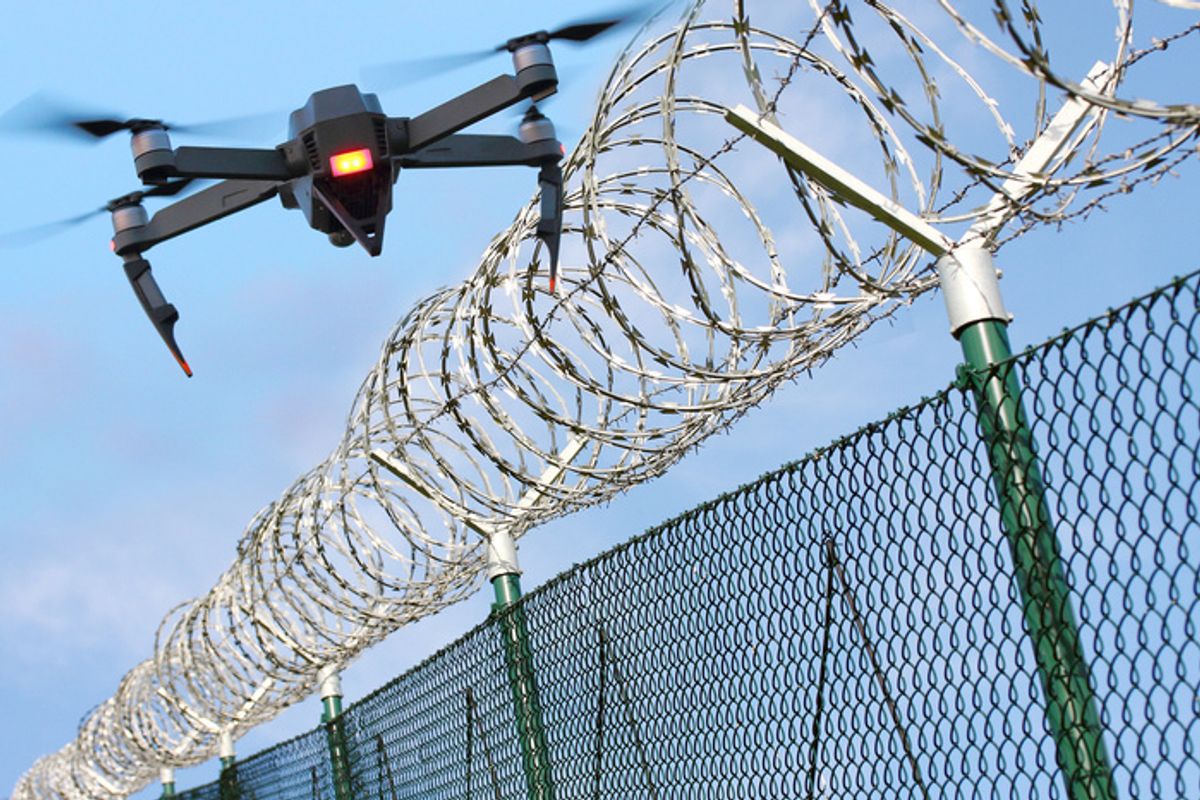 Drone with an orange light on the front, hovering over a barbed wire fence