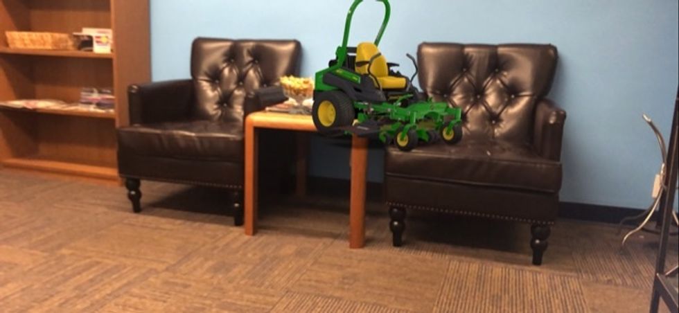 An AR image of a lawn mower sitting on top of a chair and table in a den