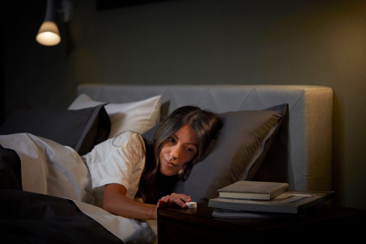 A woman waking up in bed, pushing a small white button on her bedside table