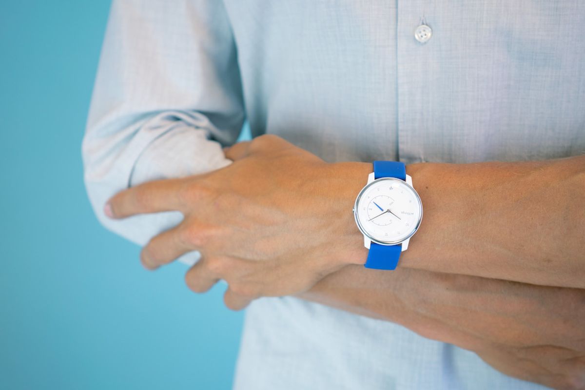 A watch with a blue band, white watch face, on an arm with shirt sleeves pushed back