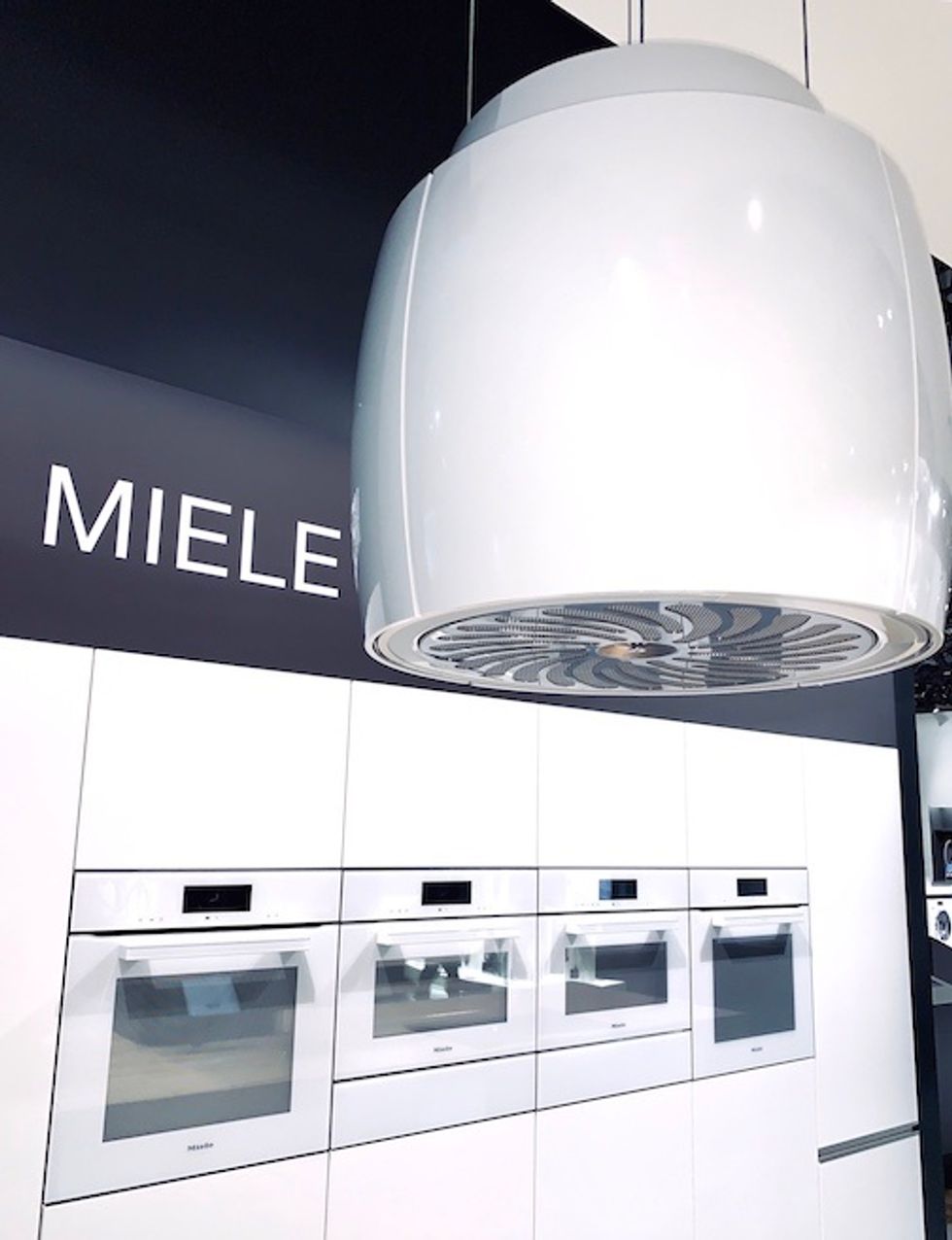 A large white kitchen hood in front of four wall ovens