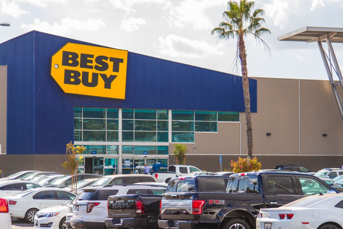 The exterior of a Best Buy store with cars parked in a lot in front of it