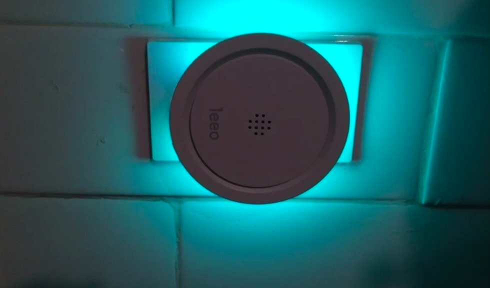 A device plugged into an outlet, shining blueish green against white tile