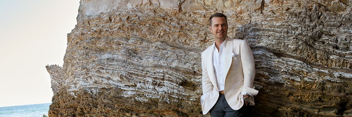 Chris O'Donnel wears white blazer and poses against a rocky outcropping.
