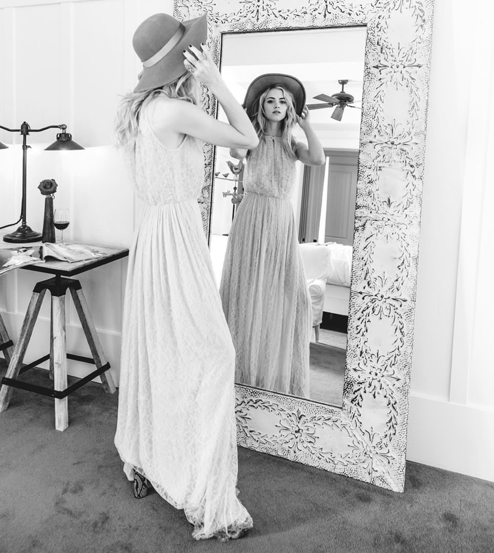 Emily Wickersham poses in a flowing dress and sunhat in front of a full-length mirror.