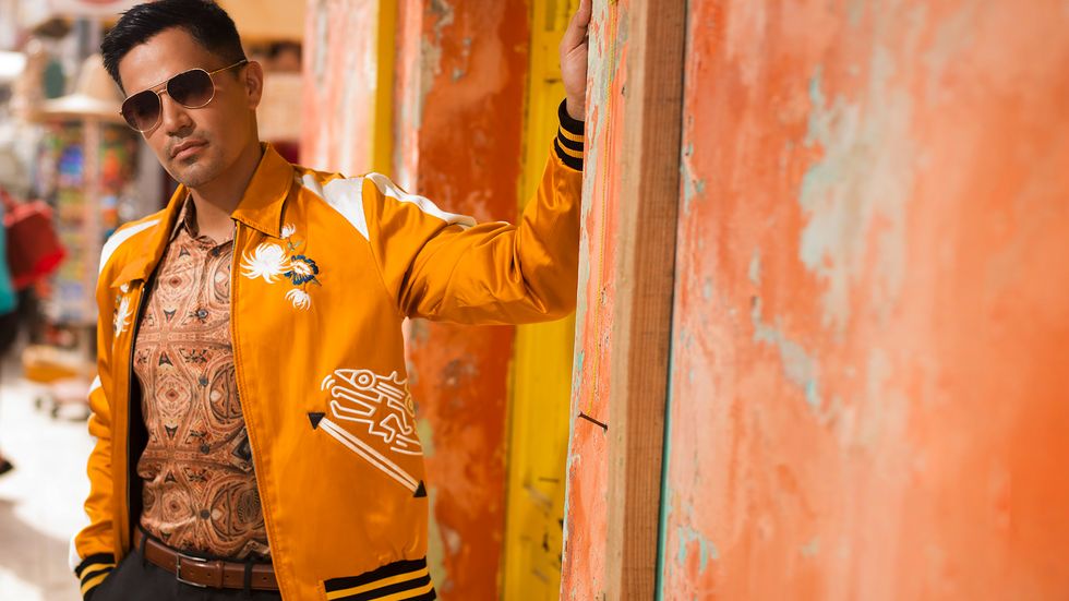 Jay Hernandez of Magnum P.I. wears an orange jacket and sunglasses