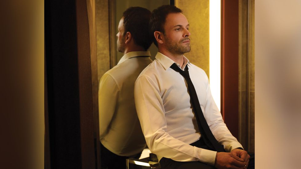 Johnny Lee Miller black tie sitting in front of mirror